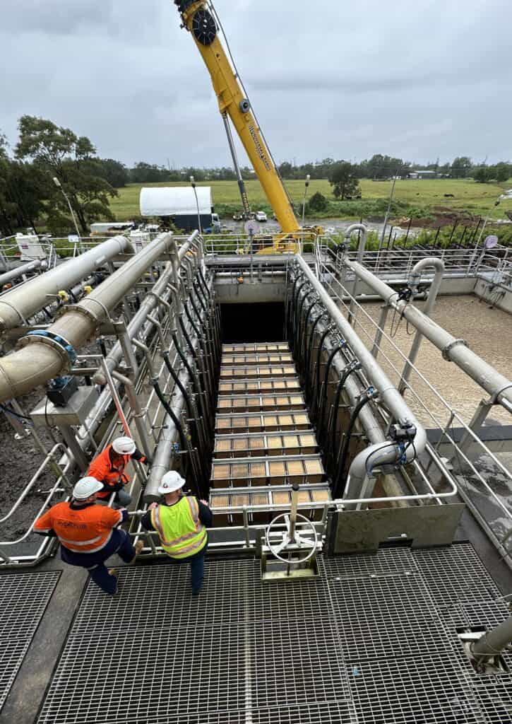 Industrial water treatment facility with engineers inspecting equipment and large crane in backgroun.