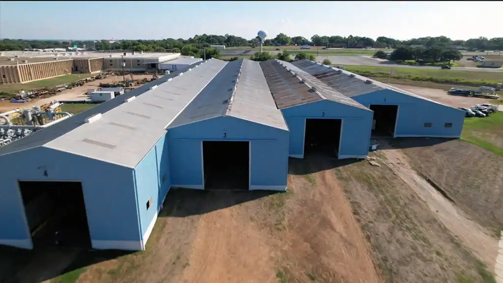 Large industrial warehouse building with multiple bays, painted blue, situated in an open area with.